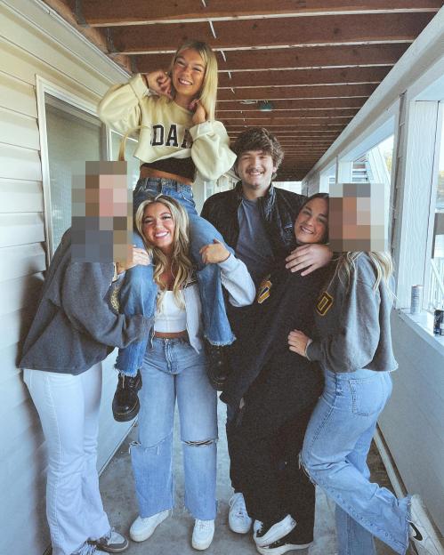 Group photo of five young adults on a porch, two women with blurred faces, one woman sitting on another's shoulders, a man standing, and one woman hugging him.