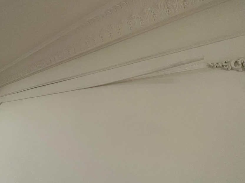 Poorly installed crown molding detached from a white wall.