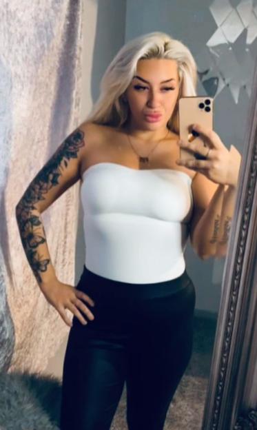 Woman in a white strapless top and black pants taking a mirror selfie with a smartphone.