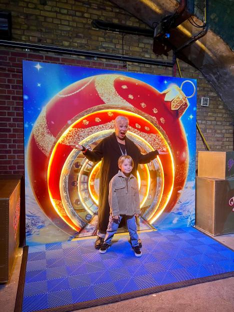 Denise Welch and Jax James posing in front of a giant Christmas ornament backdrop.