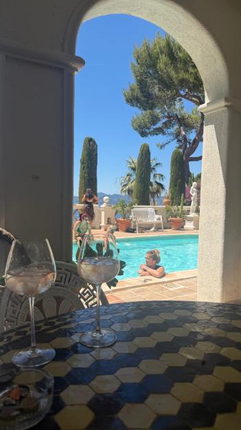 Two glasses with ice water on a hexagonal tiled table, overlooking a pool with several people.