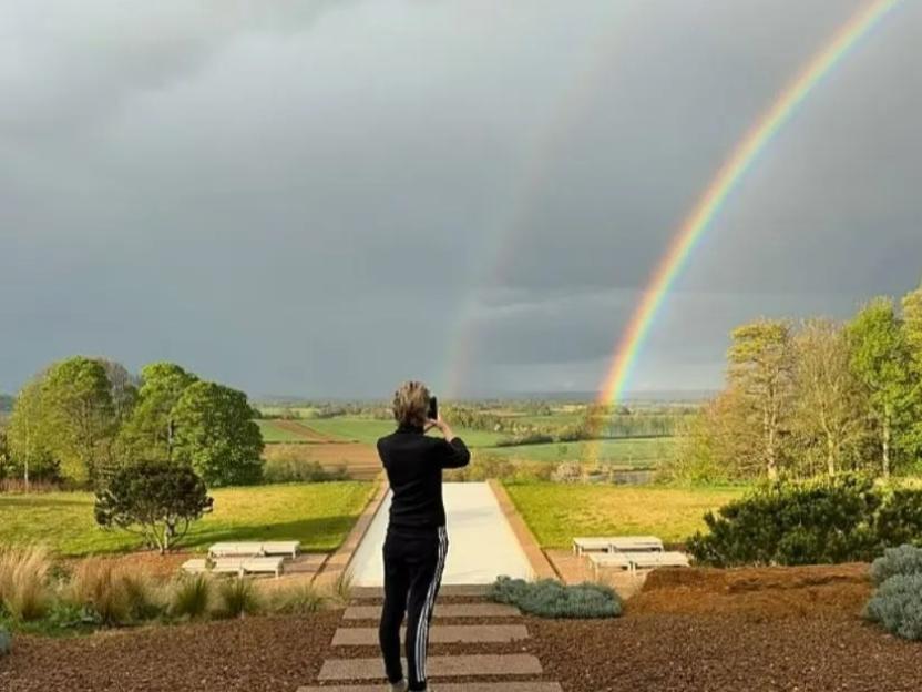 Ellen DeGeneres photographing a double rainbow over a green landscape.