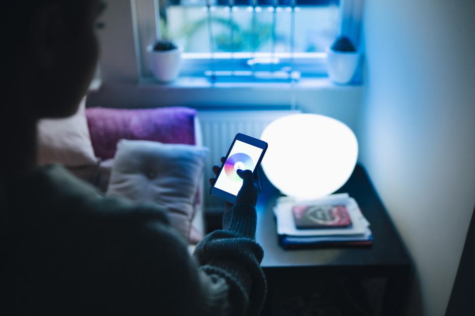 Teenage girl using a smartphone to change the color of an illuminated lamp in her room.