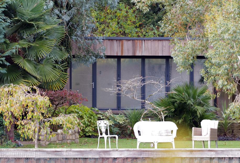 The Rolf Harris Bray Home with moss growing on the building and several white chairs on the lawn.