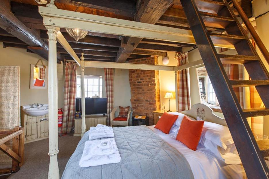 A bedroom in Cley Windmill with a four-poster bed, exposed brick and beams, and a ladder to an upper floor.