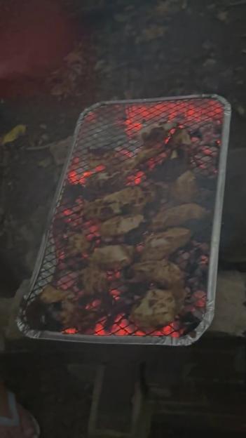 Food cooking on a portable barbecue grill with red-hot coals.