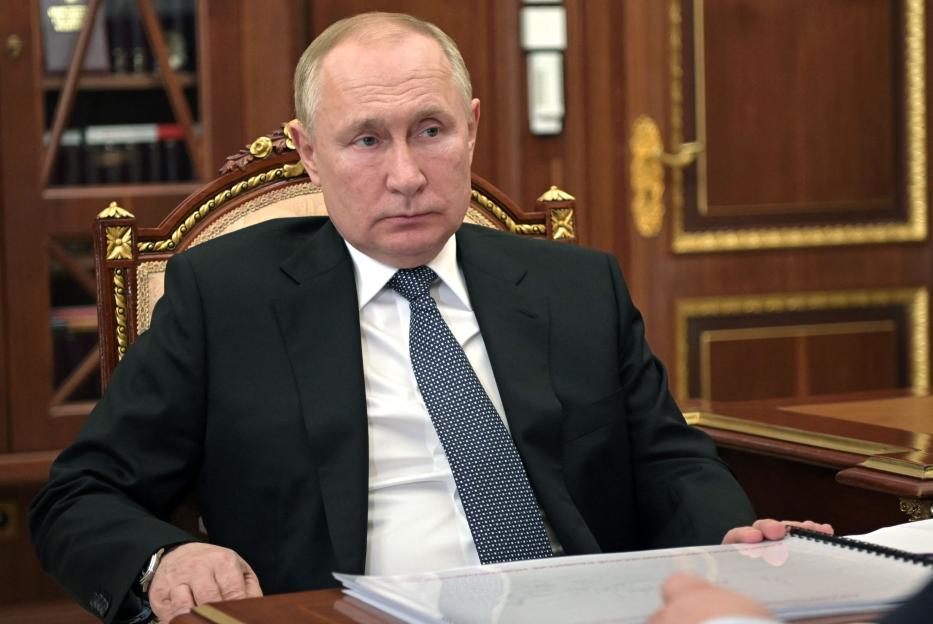 Russian President Vladimir Putin in a black suit and patterned tie, seated at a desk.