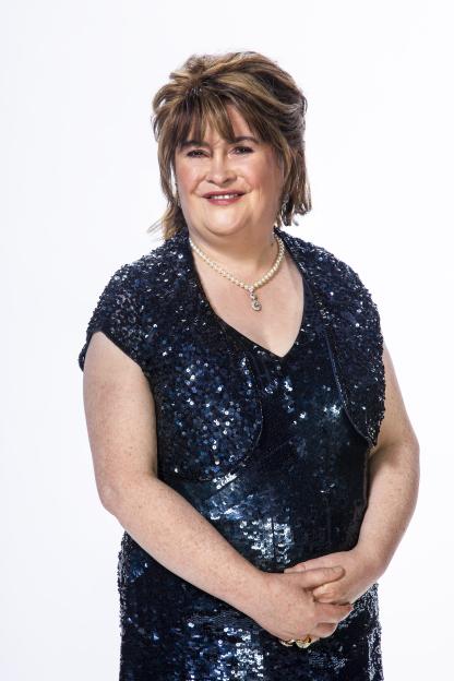 Susan Boyle smiling in a navy sequined dress and pearl necklace.