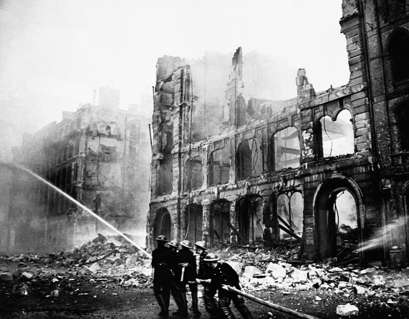 Firefighters battling blazes in a destroyed city street during the Battle of Britain.