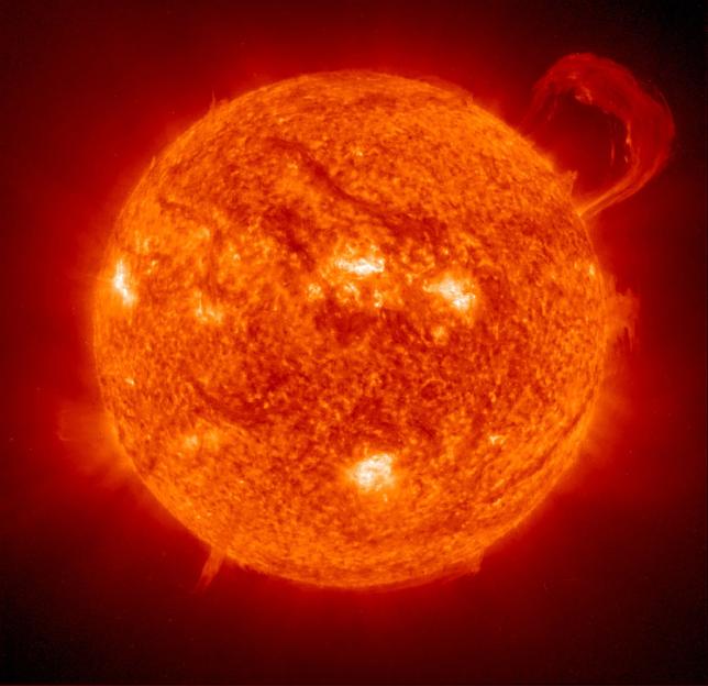The Sun, a sphere of orange and red, with bright active regions and a prominent flare erupting from its upper right limb.