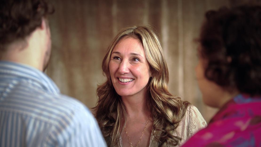 Nicole Daedone smiling at a man in a documentary scene.