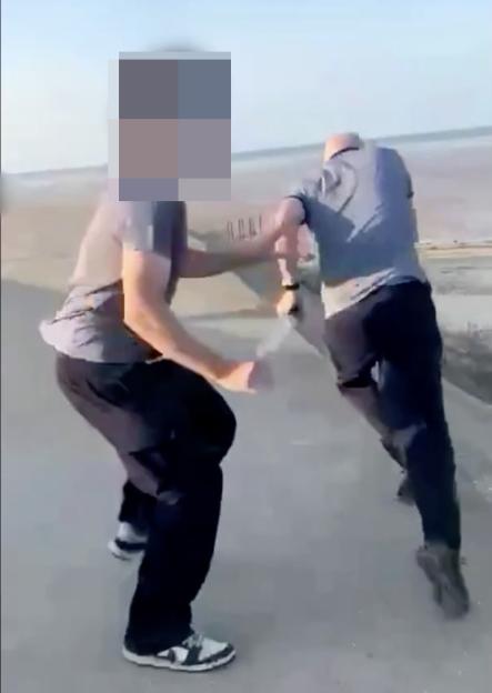 Two men in dark pants and t-shirts, with their faces blurred, in a physical altercation.