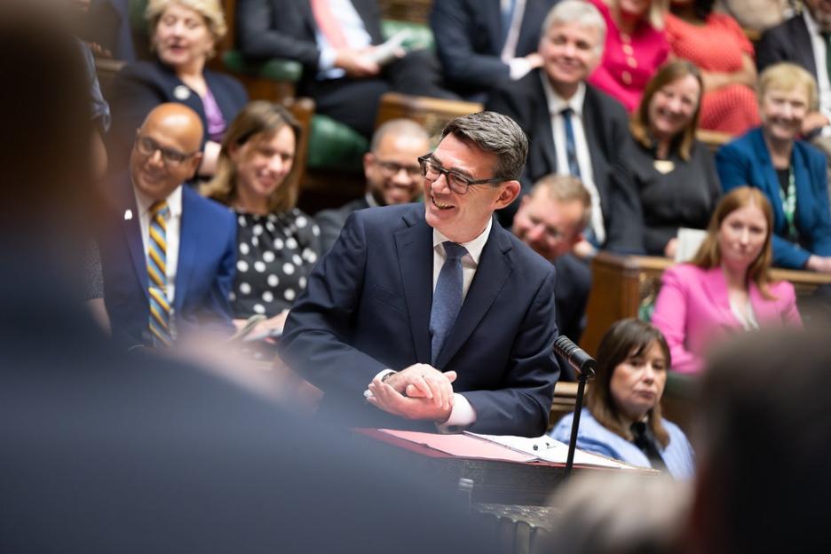 A man in glasses and a suit, speaking and smiling at Prime Minister's Questions in the House of Commons.