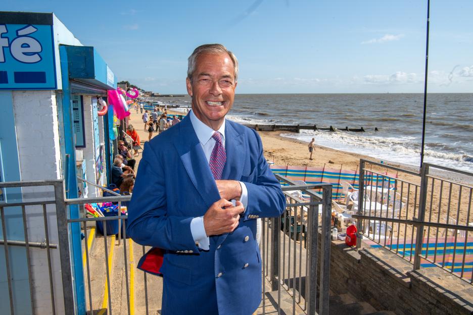 Nigel Farage, leader of Reform, smiling at the camera from a beachside cafe.