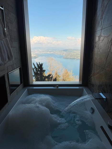 A bubble bath with a scenic view of a lake and city from a large window.