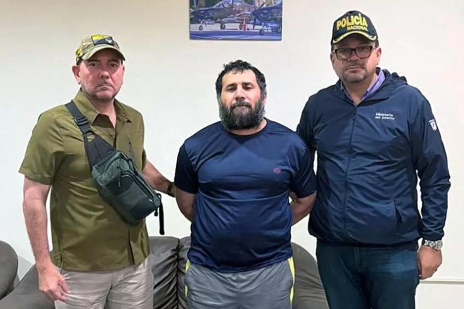 Three men, one of whom is handcuffed, posing for a photo.