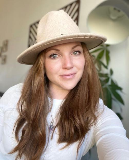 A woman with long red hair and a light-colored hat looks at the camera.
