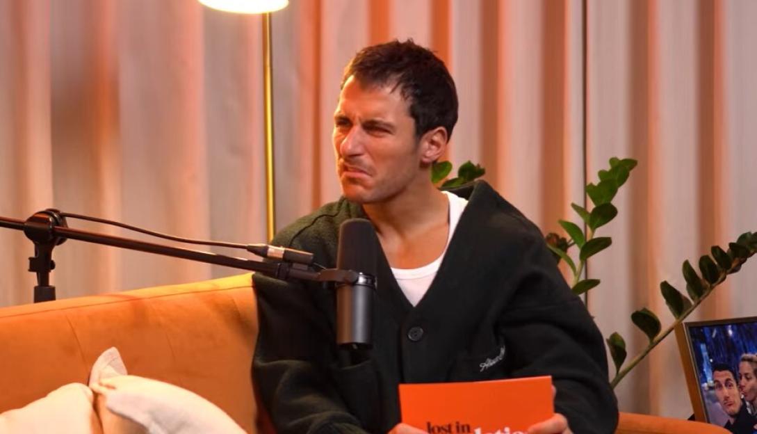 Man wincing in discomfort while holding an orange book that says "lost in notion" on an orange couch.