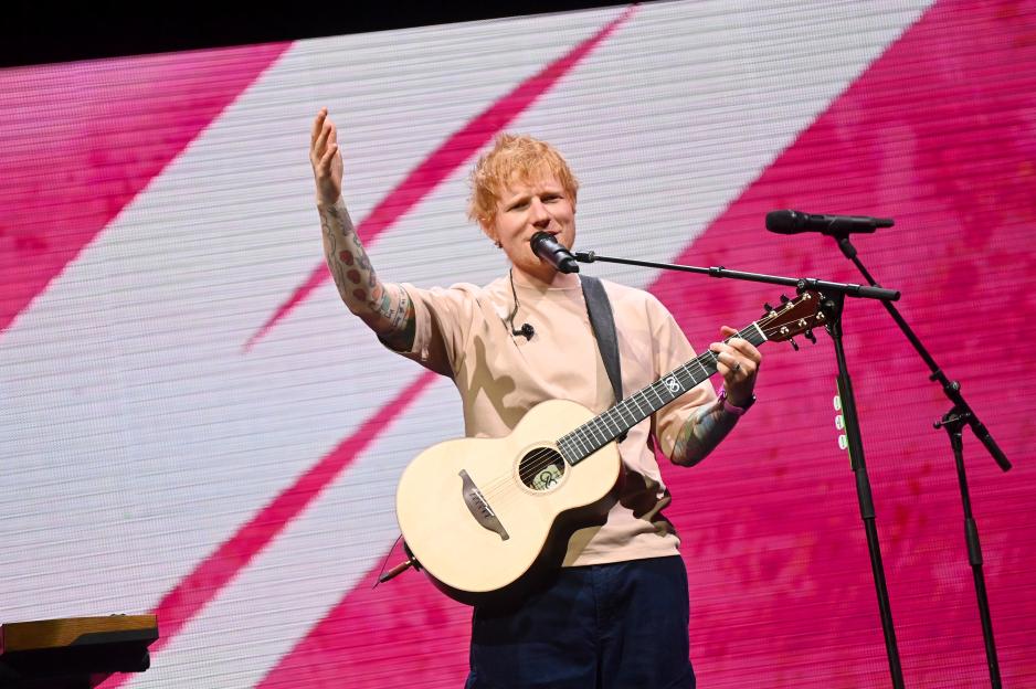 Ed Sheeran performing on stage with a guitar and microphone.