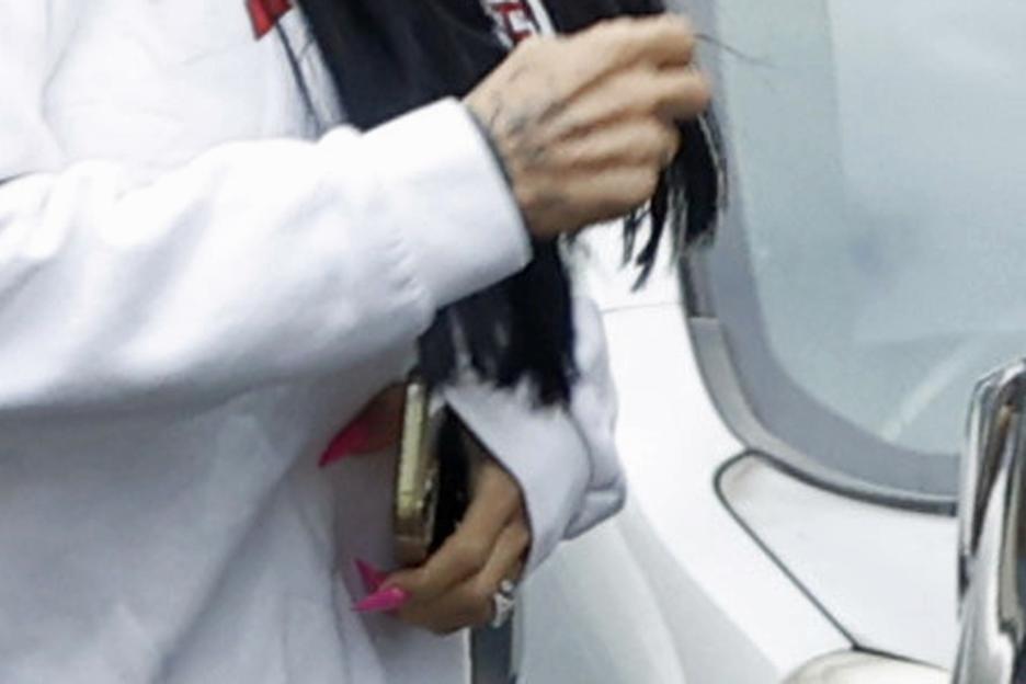 Katie Price's hand, with a wedding ring, pink nails, and a gold phone.