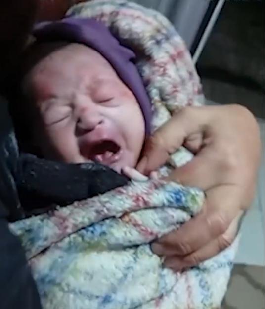 A crying newborn baby wrapped in a blanket.