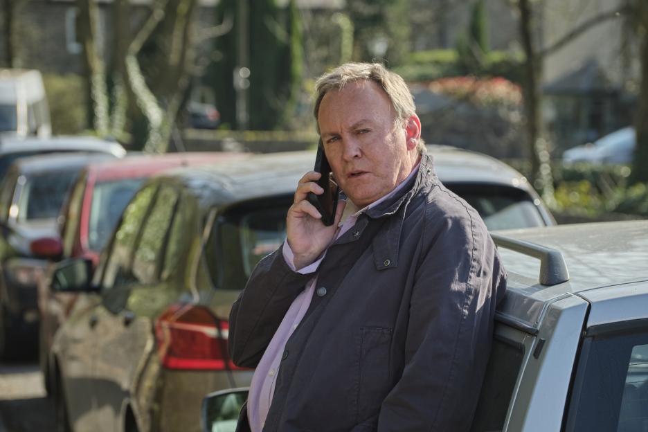Philip Glenister as Jack Radcliffe leaning on a car while on the phone.
