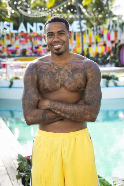 Tyrique Hyde smiling with arms crossed in yellow shorts by a pool.