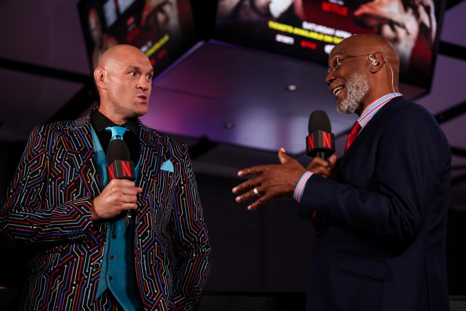 Tyson Fury and Lennox Lewis holding microphones with Netflix branding at a press conference.