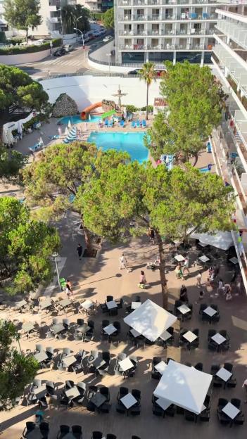 Overhead view of a hotel pool area with sunbeds and an adjacent outdoor dining area with tables and chairs.