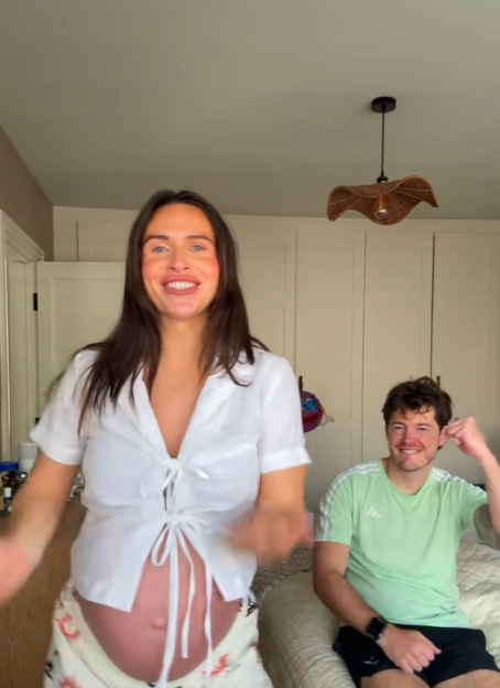 Imogen Horton showing her pregnant belly while dancing on TikTok, with a man sitting behind her.