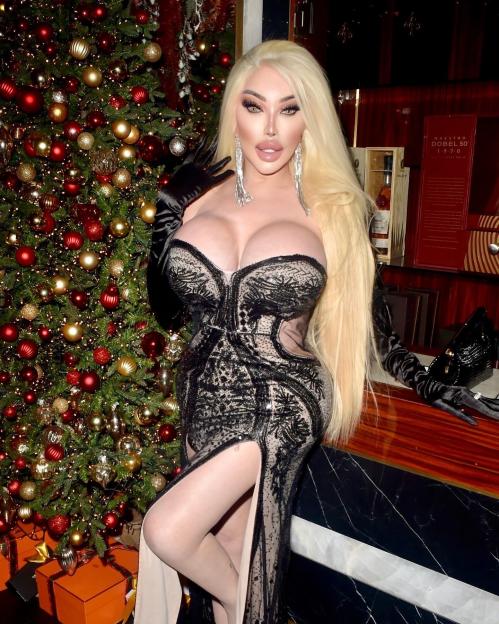 Jessica Alves posing in a black lace dress next to a Christmas tree.