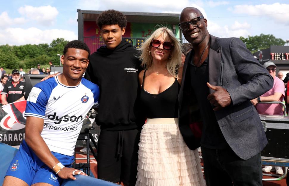 A rugby player in a white and blue jersey posing with a family and a man in a blazer.