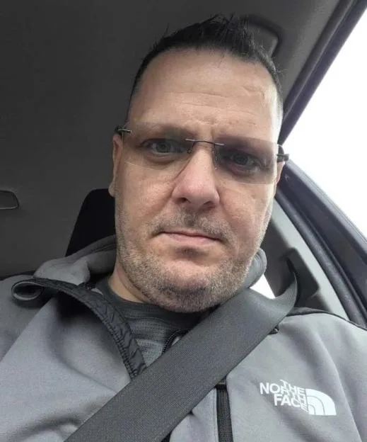 Photo of James sitting in a car wearing glasses and a grey North Face jacket.