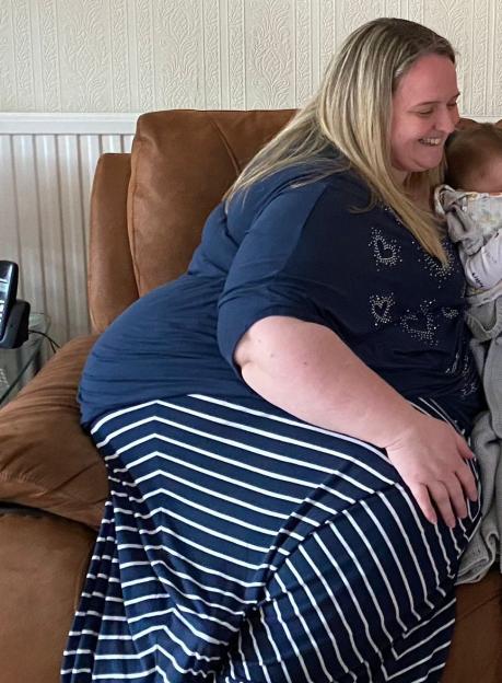 Woman in striped skirt holding baby on brown couch.