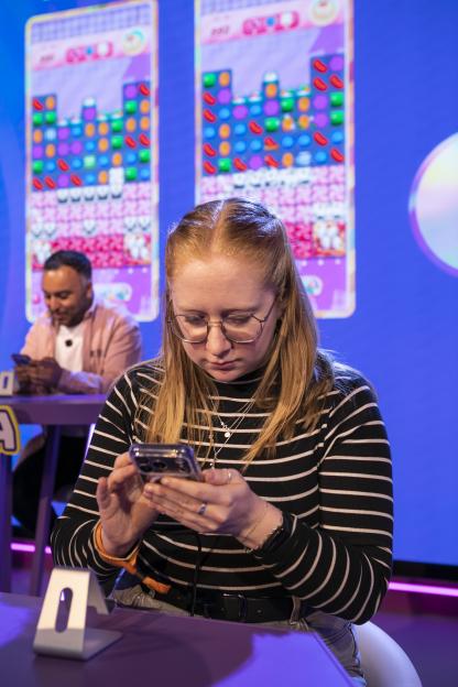 A woman looking down at her phone with Candy Crush gameplay on screens in the background.