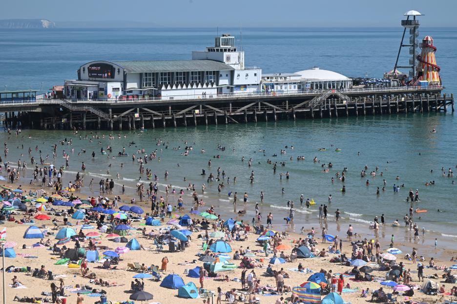 Sunbathers and swimmers fill Bournemouth beach near a pier on a hot May day.