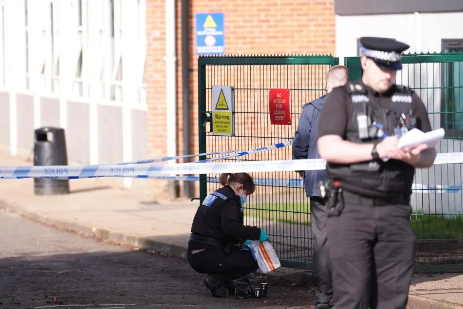 Police officers gather evidence at a school crime scene cordoned off with police tape.