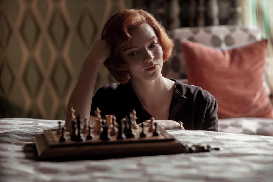 Anya Taylor-Joy as Beth Harmon in The Queen's Gambit, looking down at a chessboard with her hand on her head.