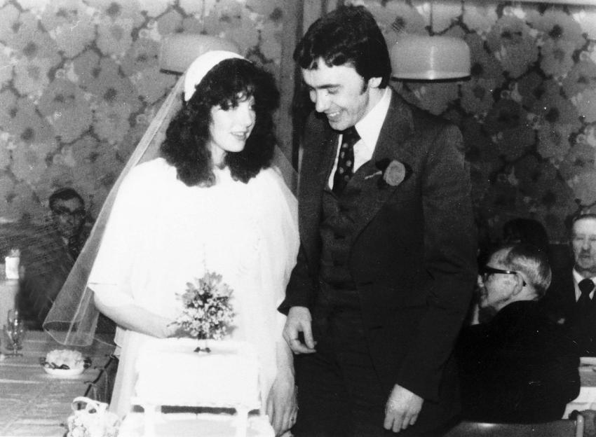 A black and white photo of Sheila Caffell and Colin Caffell at their wedding, standing by the wedding cake.