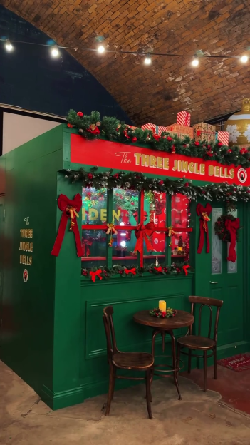 A Christmas-decorated green pub facade with the name "The Three Jingle Bells" under a brick archway.
