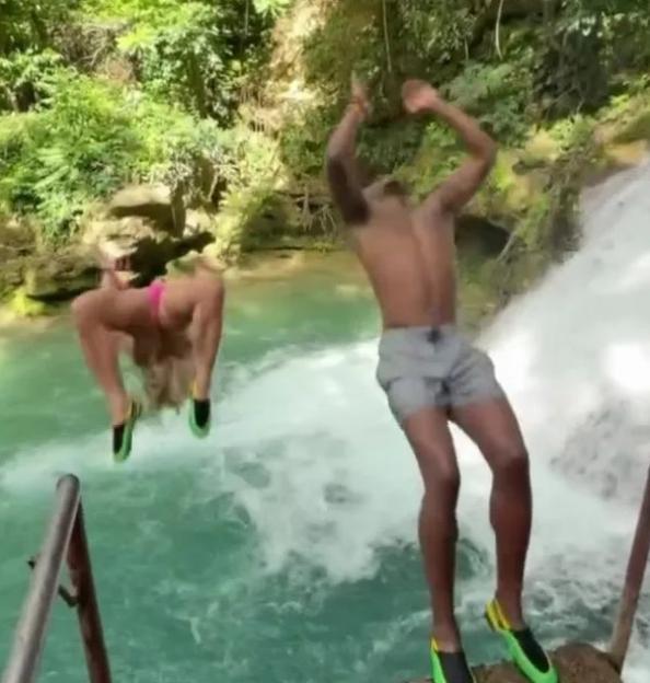 Two people jumping into a blue lagoon from a waterfall.