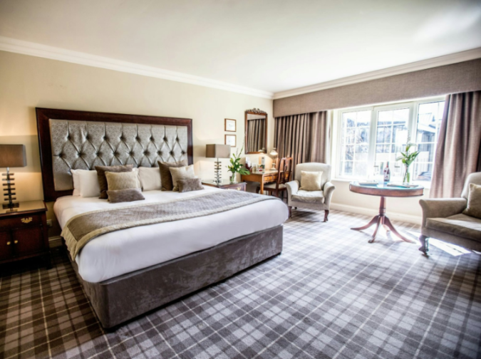 A spacious hotel room with a large bed, two armchairs, and a writing desk.