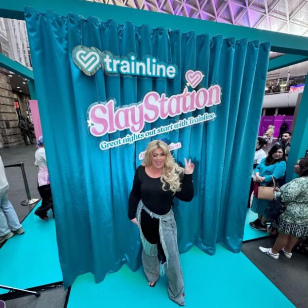Gemma Collins posing in front of a Trainline "SlayStation" backdrop.