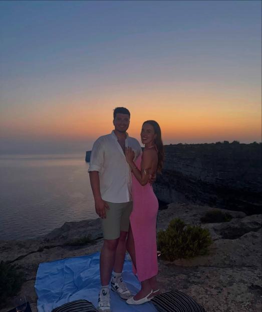 Evanna Maxted and her husband posing on a cliff overlooking the ocean at sunset.