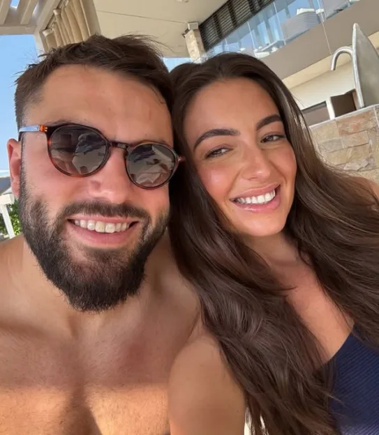 A man in sunglasses and a woman with long dark hair smile at the camera.