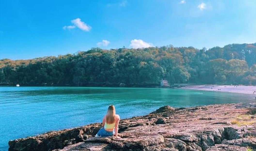 A person sitting on a rocky shore overlooking Elberry Cove.