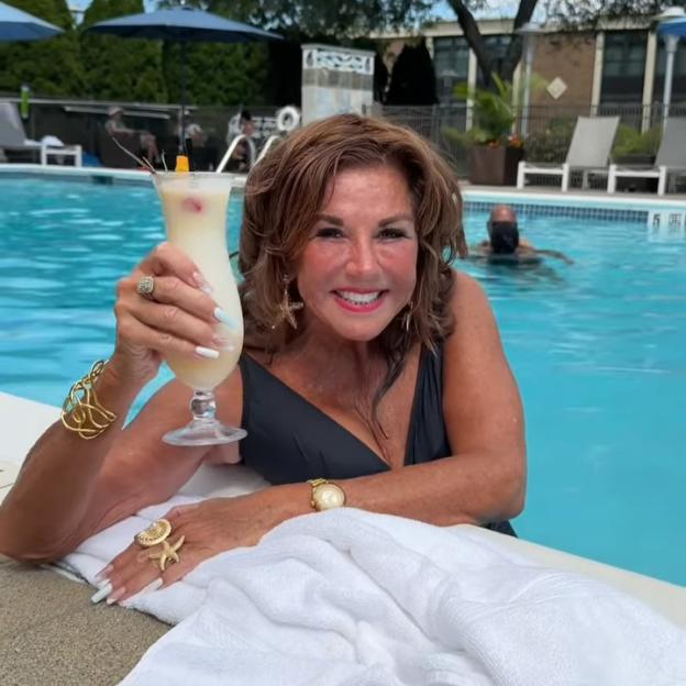 Abby Lee Miller in a swimsuit, holding a drink by a pool.