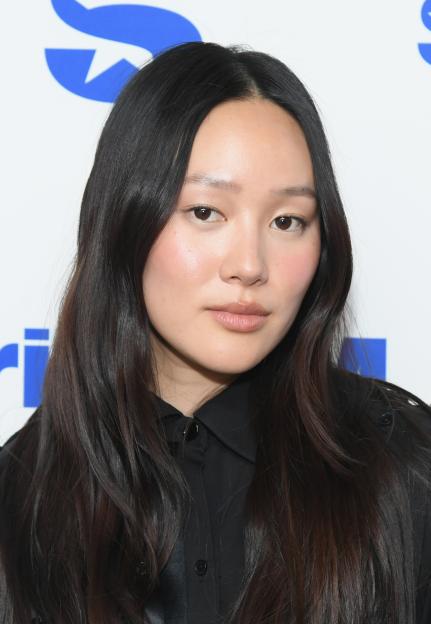 Yerin Ha with long dark hair, wearing a black shirt, posing in front of a white background with a blue SiriusXM logo.