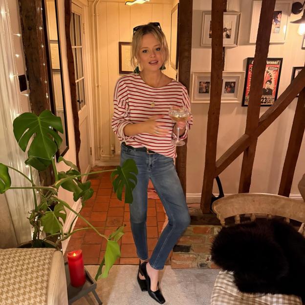 Emily Atack in a red and white striped shirt and jeans, holding a drink.