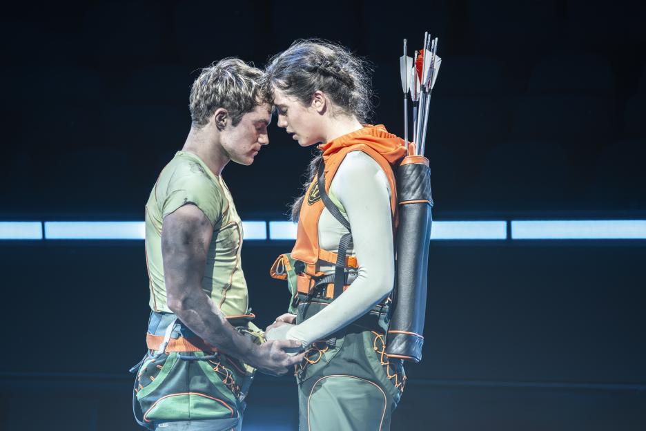 Euan Garrett as Peeta Mellark and Mia Carragher as Katniss Everdeen, facing each other with foreheads touching.